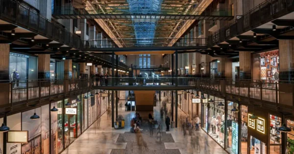 Modern shopping centre interior with glass roof, multiple levels, and retail stores.
