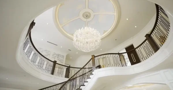 Luxury home interior with a grand staircase, elegant chandelier, and ornate railing under a circular ceiling.